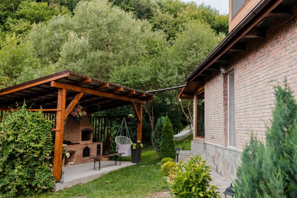 O imagine a foișorului nou construit de la Cabana Ana, cu un grătar din cărămidă și un cuptor pentru pâine. Se observă acoperișul de lemn, o bancă de relaxare, un leagăn suspendat și o parte din exteriorul cabanei. Spațiul este înconjurat de vegetație luxuriantă.
