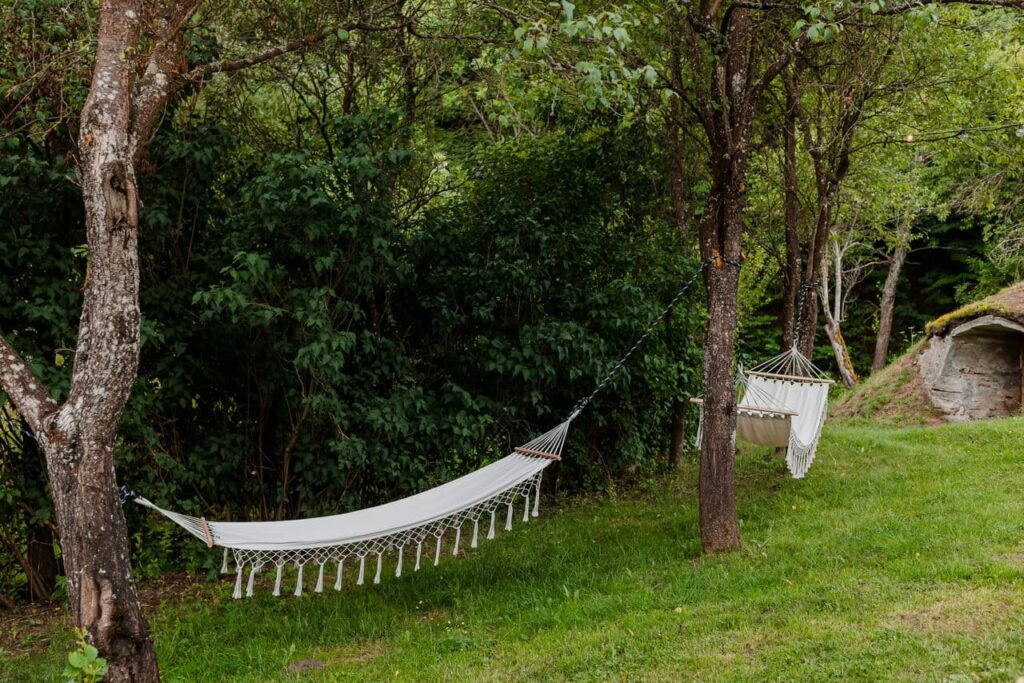 O imagine din grădina Cabanei Ana, cu două hamace albe, agățate de copaci. În fundal, se observă un deal verde, în care este săpată o intrare rustică, ce duce la cramă. Este o imagine relaxantă, care invită la odihnă în natură.
